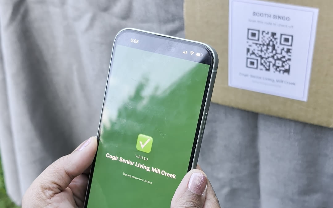 A phone confirming a MoveNSeek booth visit, with the booth's bingo QR code behind it